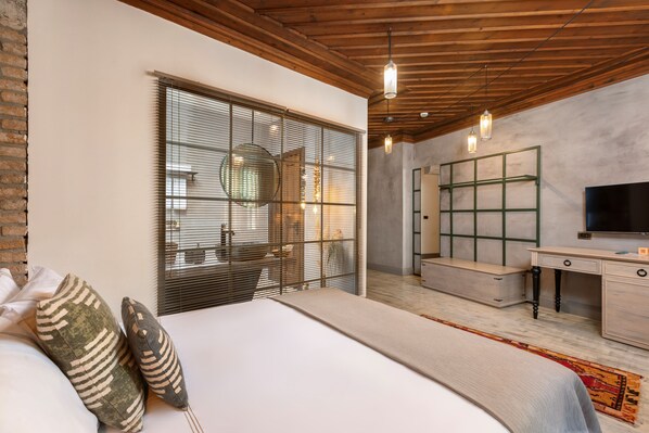 Un dormitorio moderno con una cama grande, un escritorio, un televisor y una ventana con persianas.
