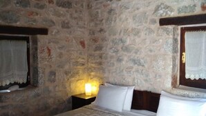 Une pièce aux murs de pierre, avec un lit, une table de chevet et une fenêtre avec un rideau.