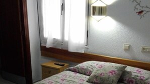 Une chambre à coucher avec une couvre-lit à motifs floraux, une table de chevet, une lampe et une fenêtre avec des rideaux.