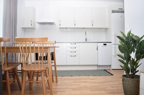 A modern kitchen with white cabinets, a wooden dining table, and a potted plant. - Företagsbostäder Skarpskyttevägen (Lund)