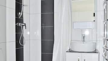 Ein modernes Badezimmer mit Toilette, einer Dusche mit gebogener Brause, einem weißen Waschbecken mit Spiegel darüber und einer schwarzen Wand aus Fliesen.