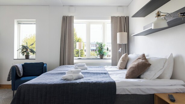 Habitación de hotel con cama, lámparas de noche, escritorio, silla y vistas al exterior.