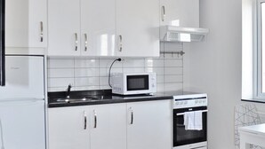 A modern kitchen with white cabinets, a microwave, an oven, and a black and white patterned rug. - Företagsbostäder Skarpskyttevägen (Lund)