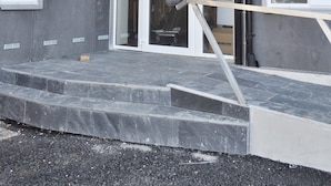 Un edificio con fachada gris, ventanas con marcos blancos y una escalera que lleva a una puerta.