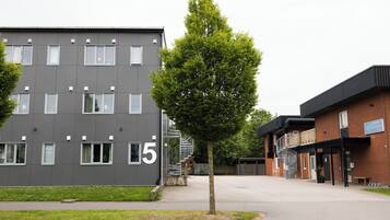 A modern building with a grey facade and multiple windows, a tree in front, and a brick building with a sign.