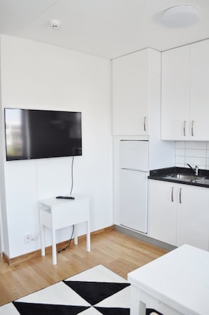 A modern kitchen with white cabinets, a built-in refrigerator, a black countertop, and a mounted flat-screen TV. - Företagsbostäder Skarpskyttevägen (Lund)