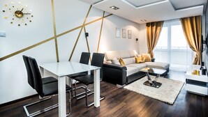 Uma sala de estar moderna com um sofá branco, cadeiras pretas, uma mesa de jantar de vidro e um design geométrico na parede.