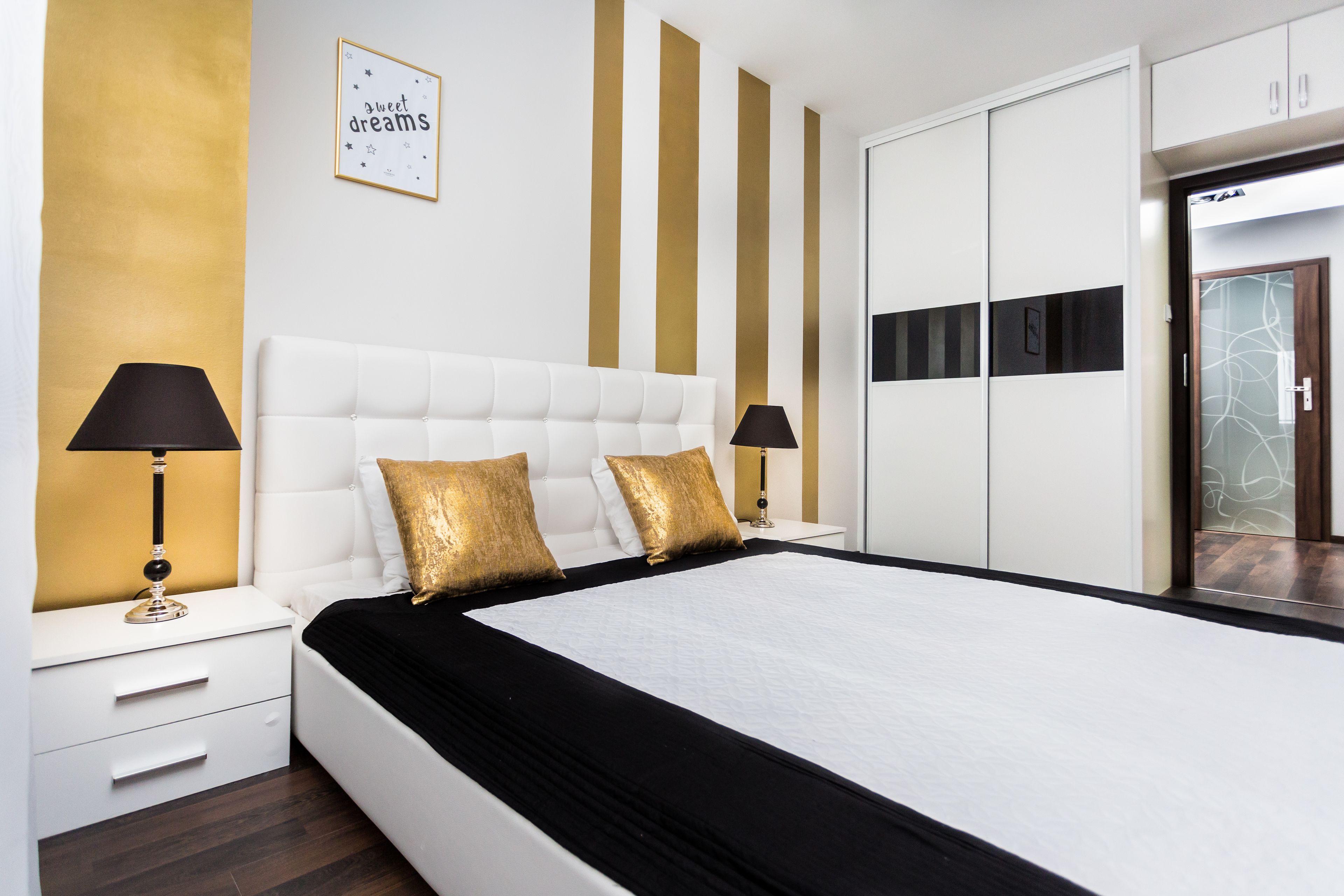 Une chambre moderne avec un grand lit, une décoration blanche et dorée, et une armoire avec un miroir.