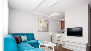 Uma sala de estar moderna com um sofá azul-turquesa, uma televisão de tela plana e uma pequena mesa branca.