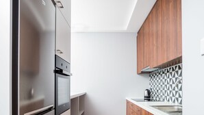 Uma cozinha estreita com armários de madeira, uma geladeira de aço inoxidável e um revestimento de azulejos.