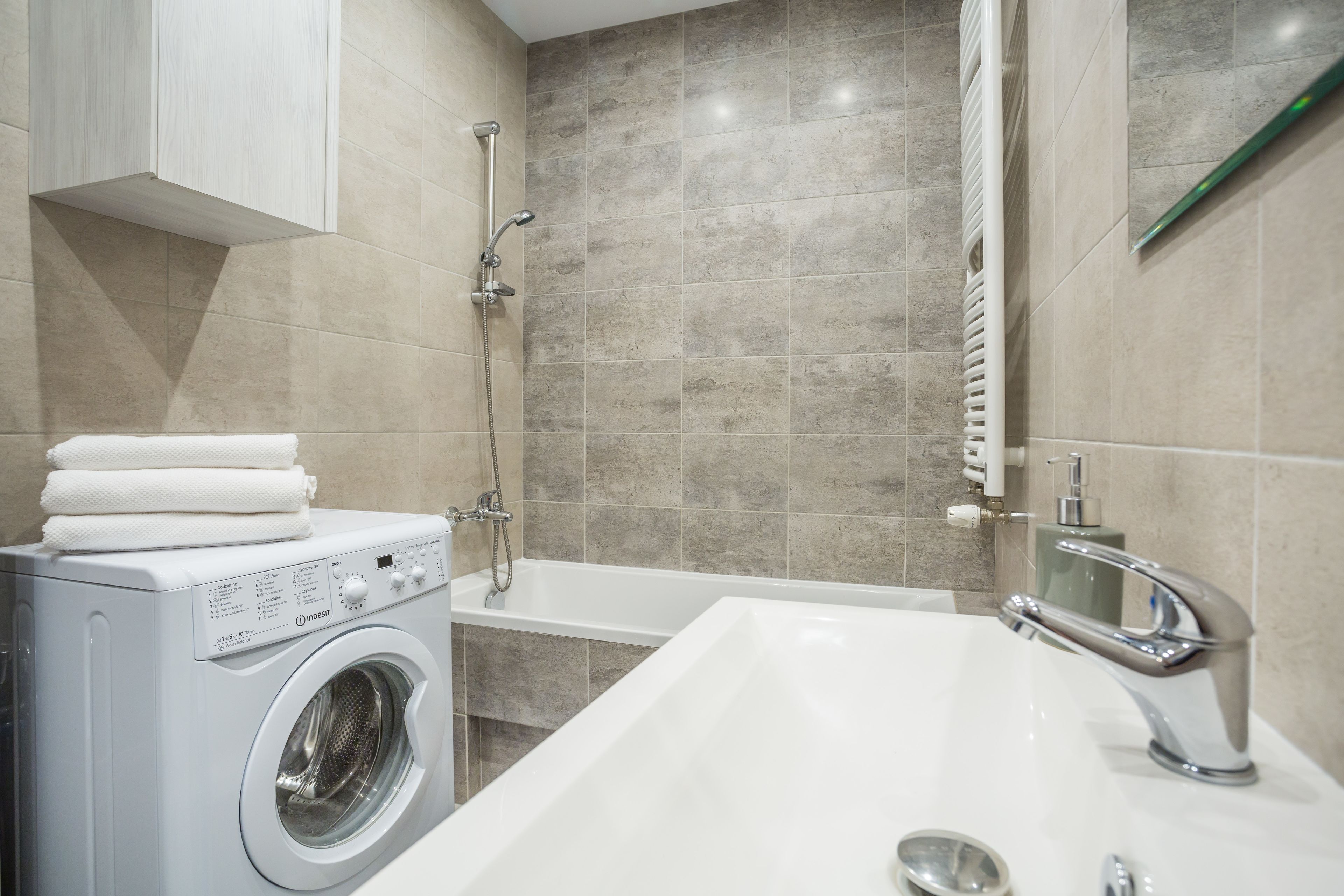 Ein modernes Badezimmer mit integrierter Waschmaschine, einer Badewanne und einem Waschbecken mit Armatur.