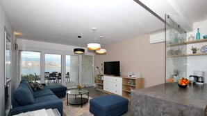 Ein modernes Wohnzimmer mit einem blauen Sofa, einem Glastisch und einem Fernseher auf einer Holzkommode.