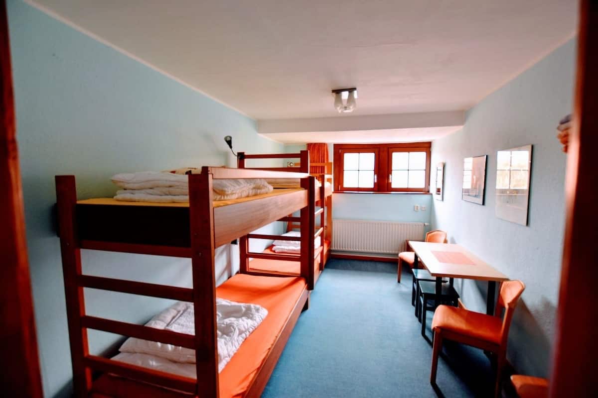 Un dormitorio con literas, una mesita pequeña, sillas y un radiador.