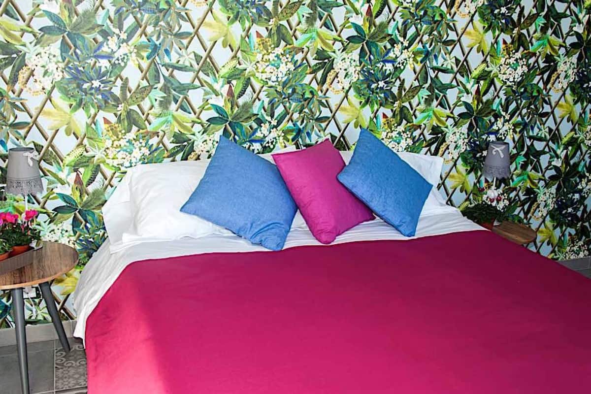 A bed with white linens, a red bedspread, and two pillows (one blue, one pink).
