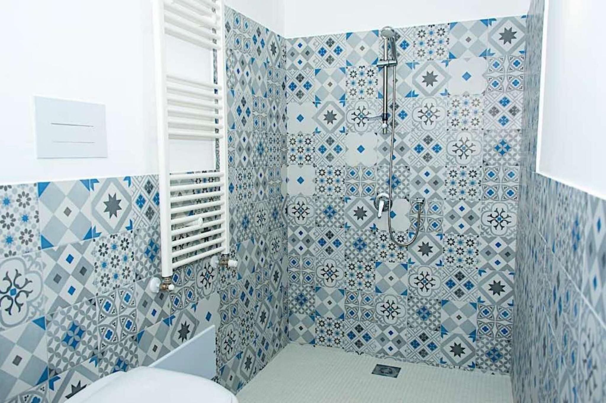 Un baño con baldosas estampadas, un radiador blanco y una ducha.