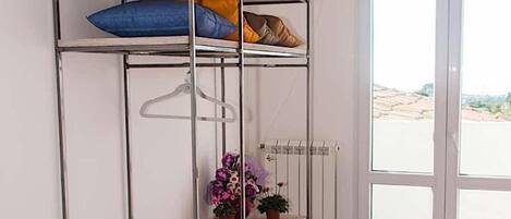A bunk bed with a metal frame and wooden shelves, a radiator, a potted plant, and a view of the outside through a glass door.