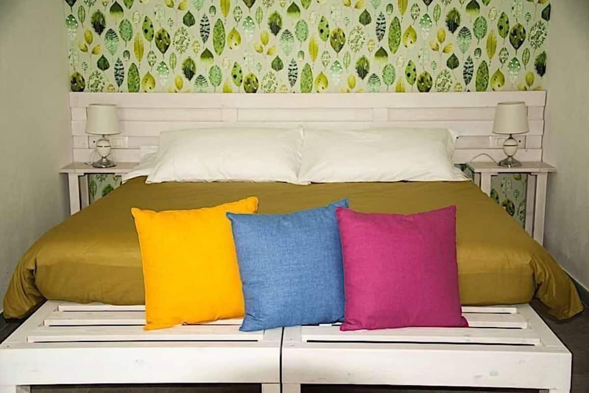 A bed with a green bedspread and three pillows in yellow, blue, and pink.