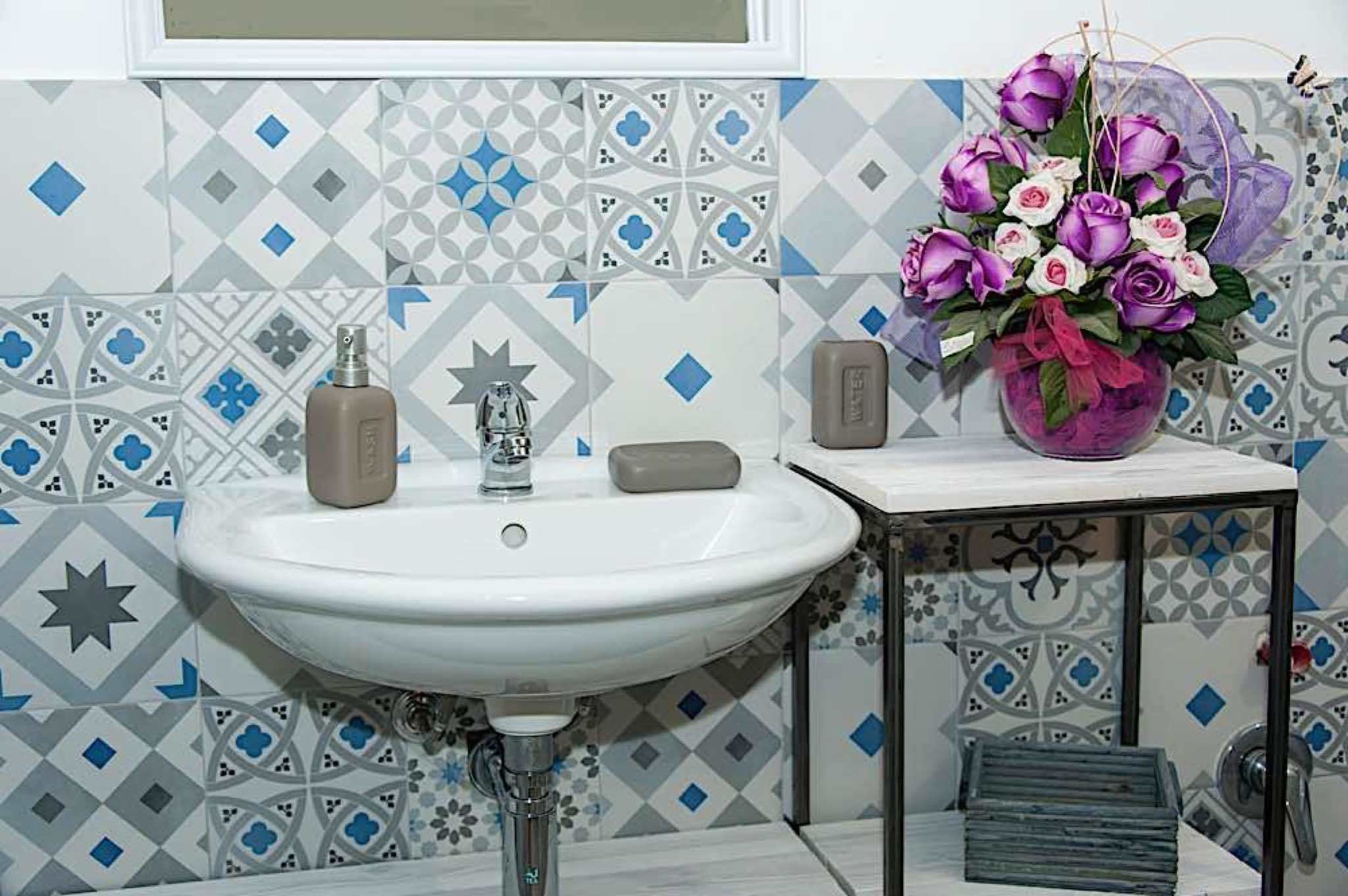 A bathroom with a white sink, a star-shaped soap dispenser, a soap bar, and a vase with purple and white flowers.
