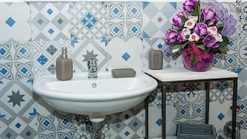 Un baño con un lavamanos blanco, un dispensador de jabón con forma de estrella, una pastilla de jabón y un florero con flores moradas y blancas.