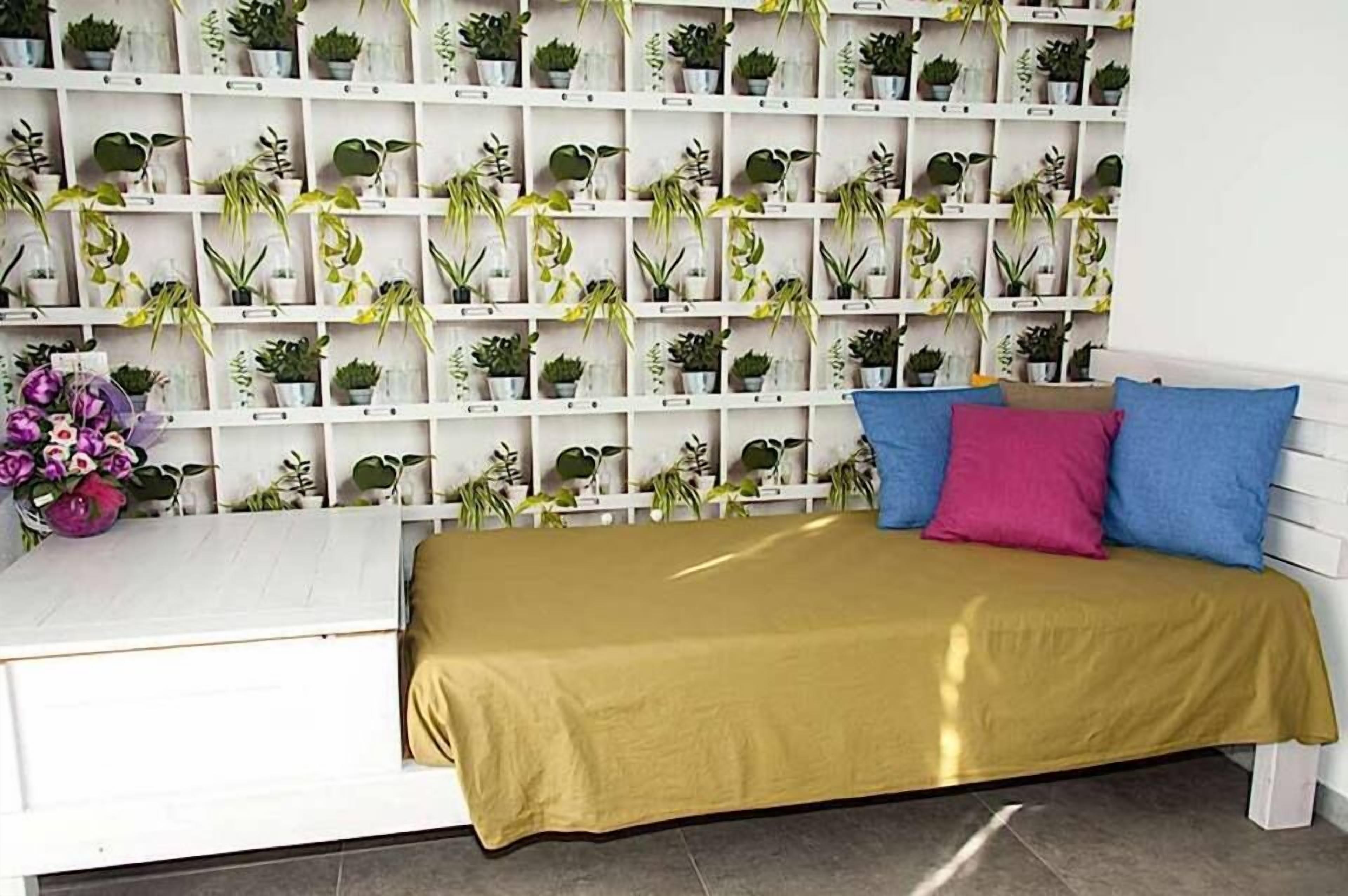 Una habitación ordenada con una cama, un escritorio blanco y una pared llena de plantas en macetas.