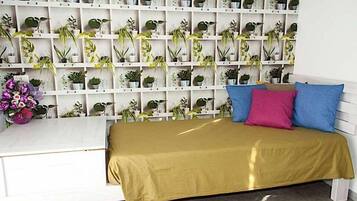 Una habitación ordenada con una cama, un escritorio blanco y una pared llena de plantas en macetas.