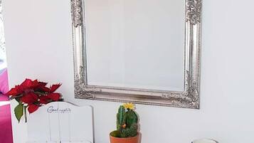 Un espejo montado en la pared con un marco decorativo, una pequeña maceta, un cartel con la palabra "RECIPES" y una taza azul sobre un mueble de madera.