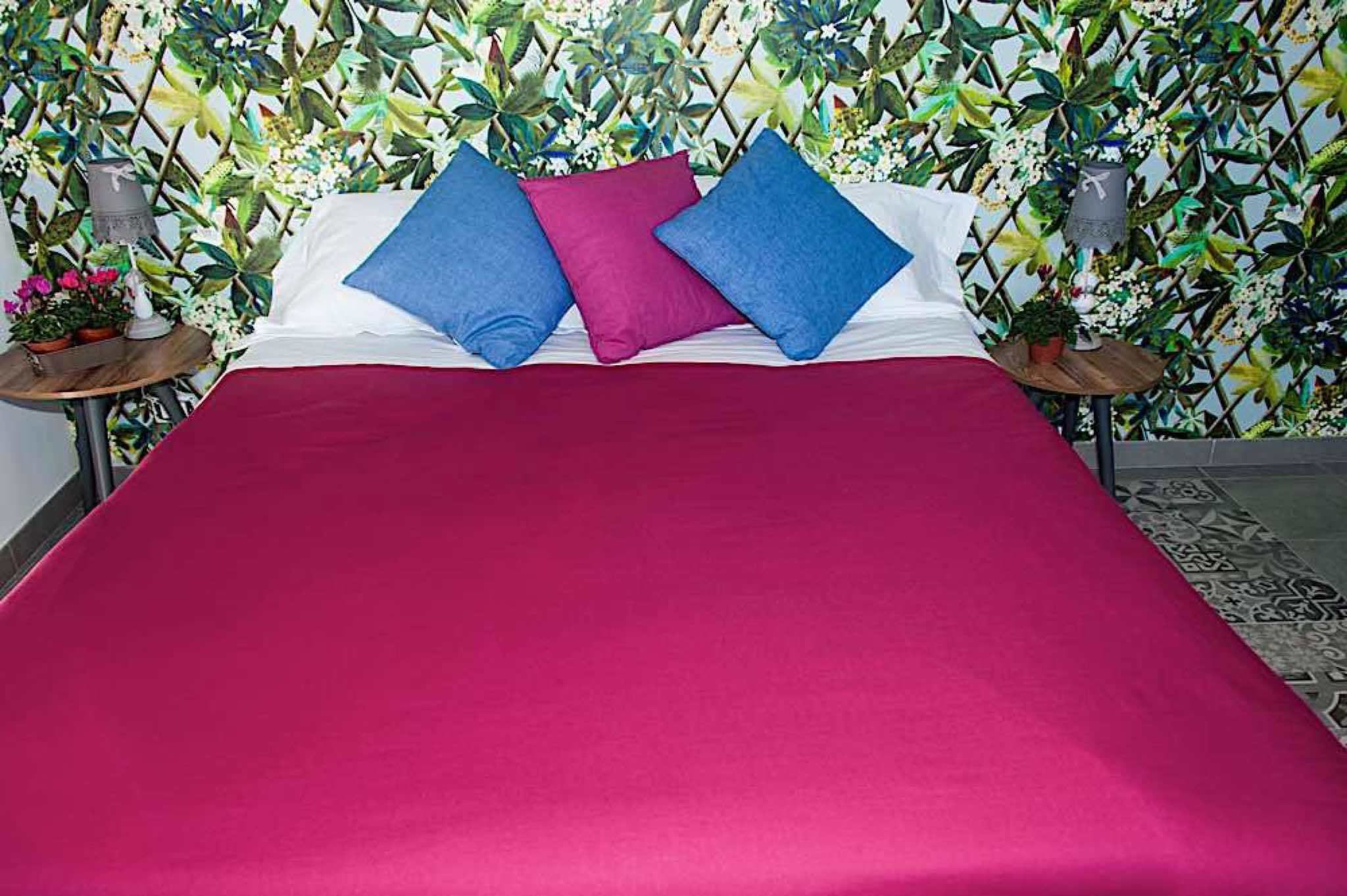 A bed with a red bedspread, two blue pillows, and one pink pillow.