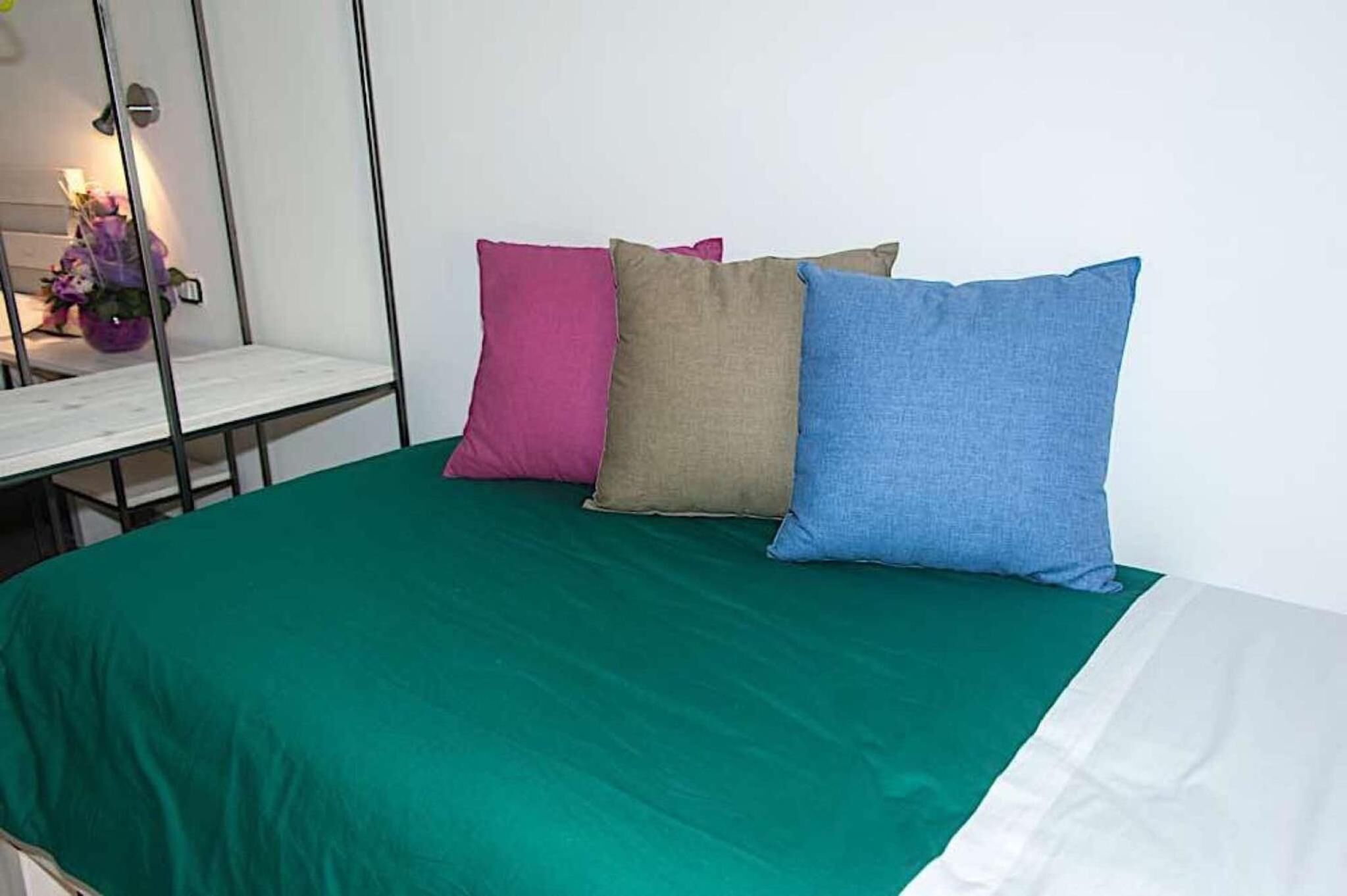 Un lit avec une couvre-lit verte et trois oreillers de couleur rose, beige et bleu.