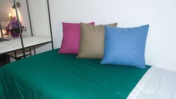 Un lit avec une couvre-lit verte et trois oreillers de couleur rose, beige et bleu.
