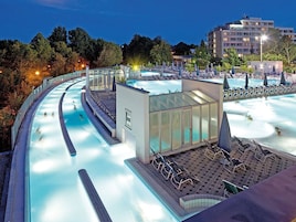 Un área de piscina hotelera con tobogán de agua, sillones de descanso y un edificio de vidrio.