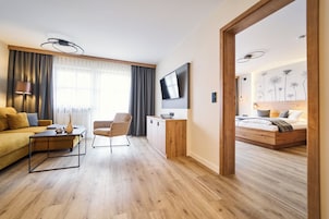 Una habitación de hotel moderna con suelo de madera, un sofá, una silla, un televisor y una cama.