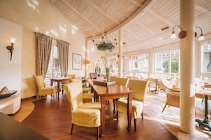 Una habitación amplia con suelo de madera, una mesa de comedor central rodeada de sillas amarillas y ventanas grandes que dejan entrar luz natural.