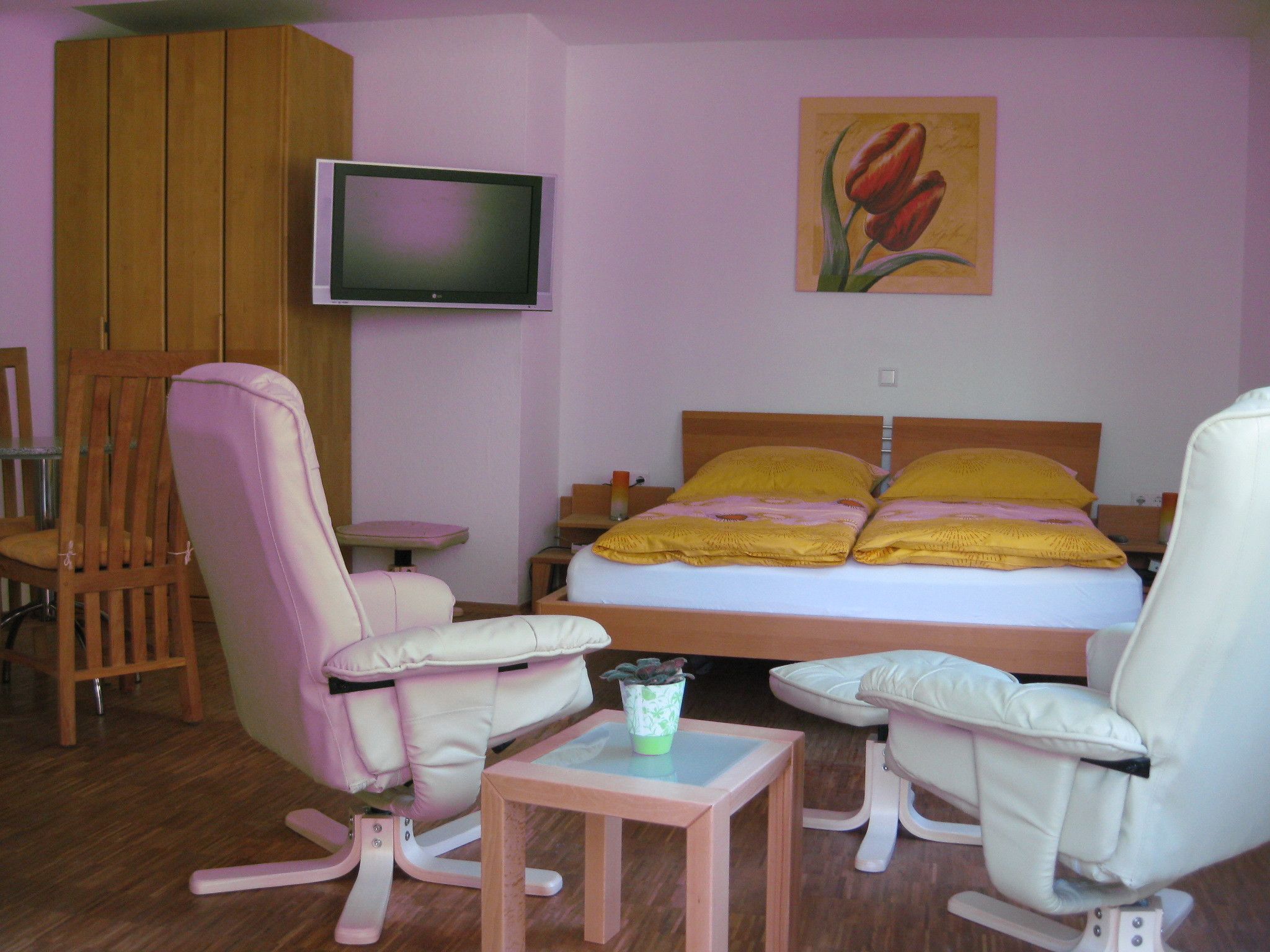 A bedroom with a bed, two chairs, a small table, a TV, and a painting.