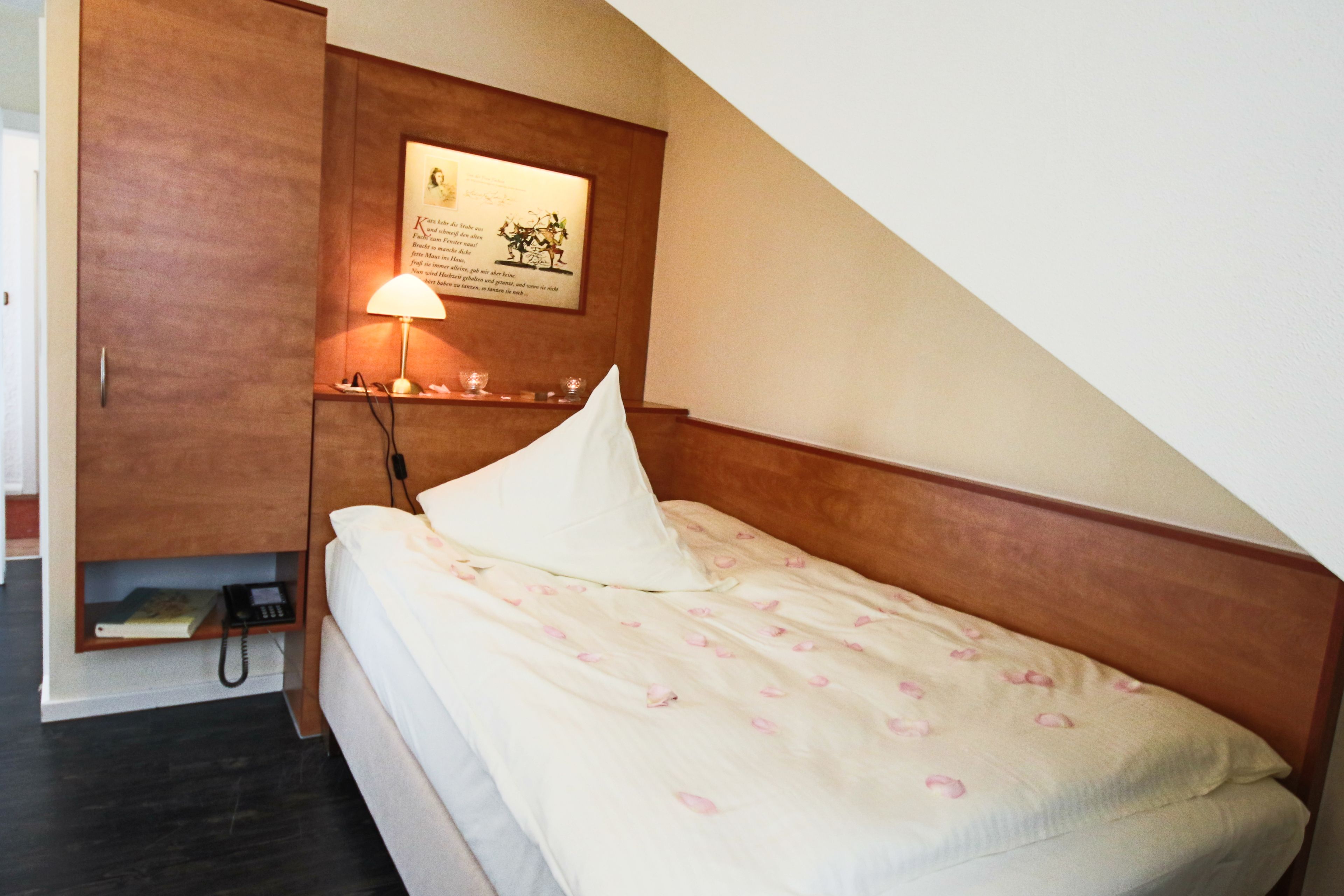 Ein Schlafzimmer mit einem Einzelbett, einer Nachttischlampe, einem Telefon und einem gerahmten Bild an der Wand.