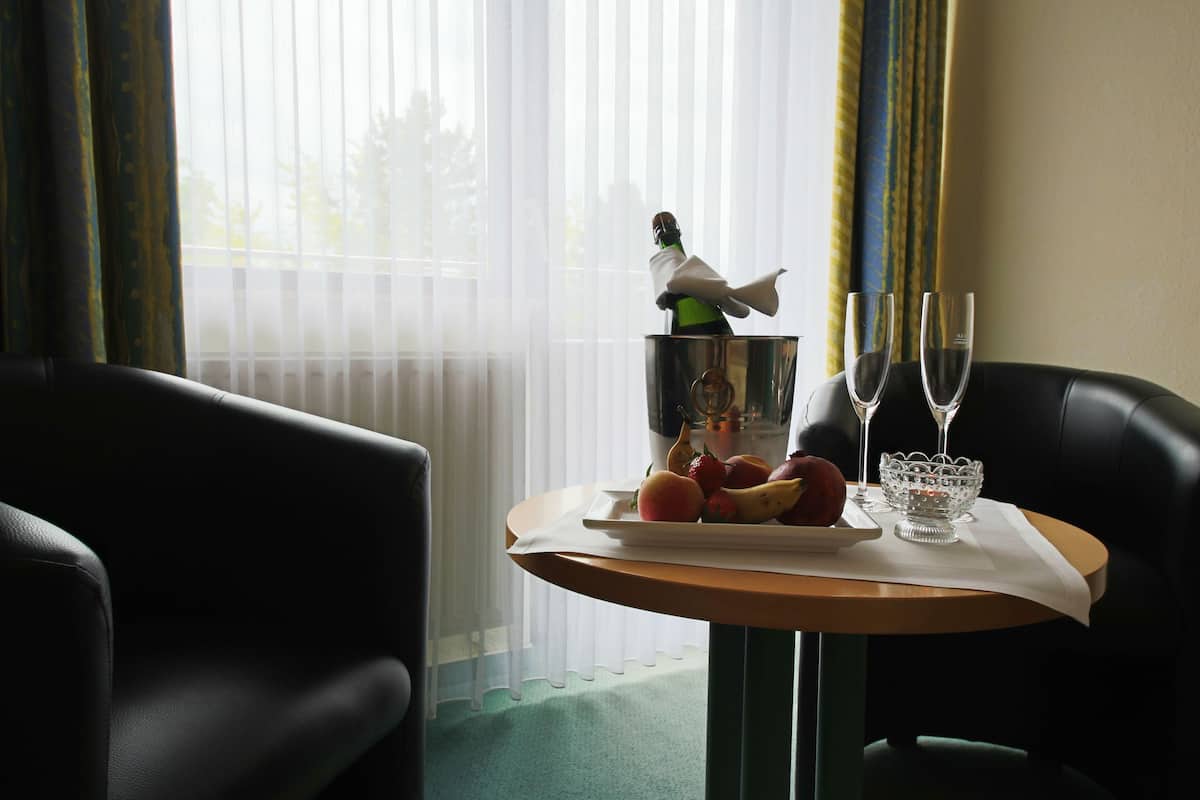 A hotel room with a table set for two, featuring a fruit platter, two wine glasses, and a decorative bottle.