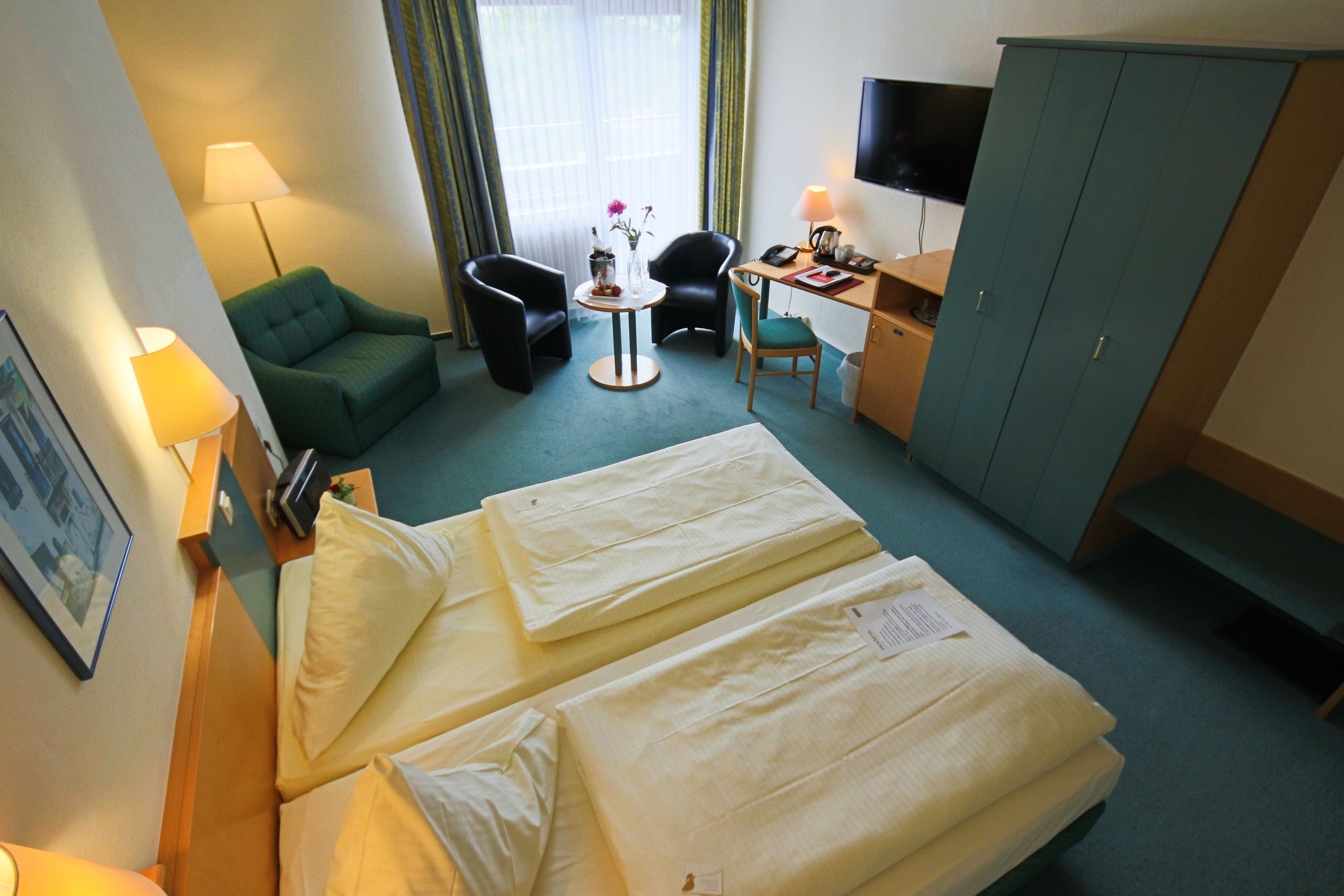 Ein Hotelzimmer mit zwei Betten, einem Schreibtisch, einem Stuhl, einem Fernseher und einer Lampe.