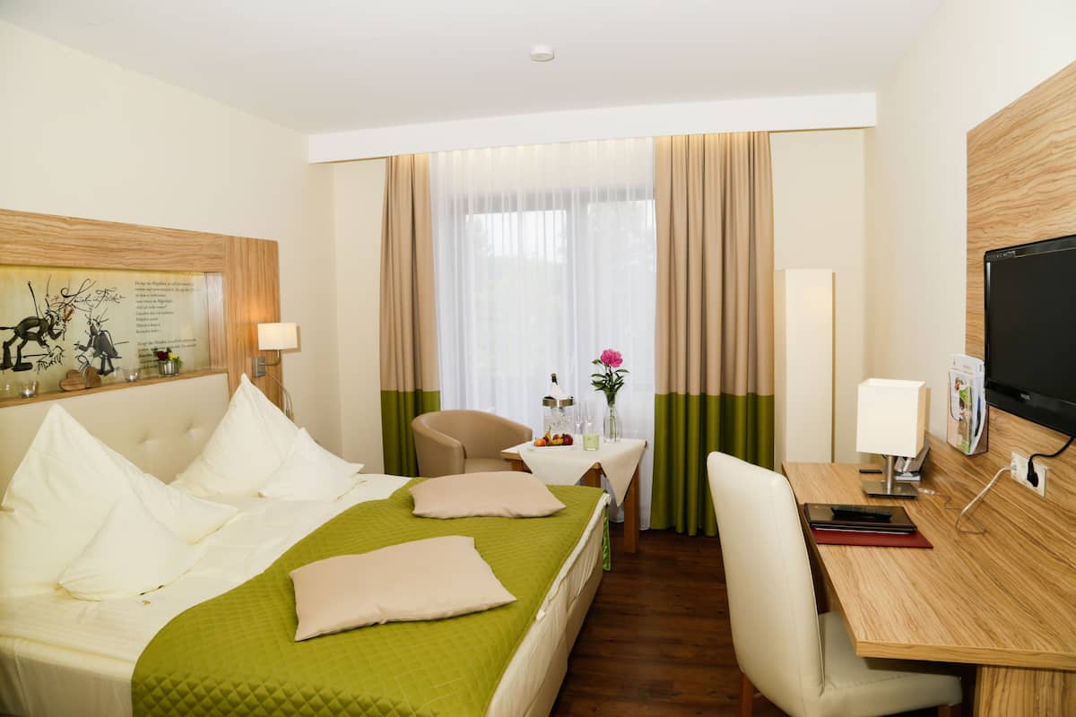 A hotel room with a bed, a desk, a chair, a TV, and a window with curtains.
