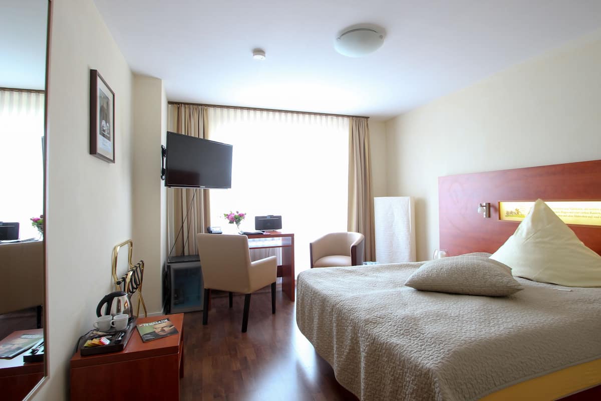 A hotel room with a bed, a desk with a chair, a television, and a window with curtains.