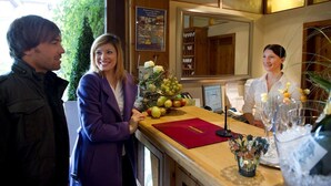 A reception area with a wooden counter, a red folder, and a display of fruits and flowers. - Parkhotel Emstaler Höhe (Bad Emstal)
