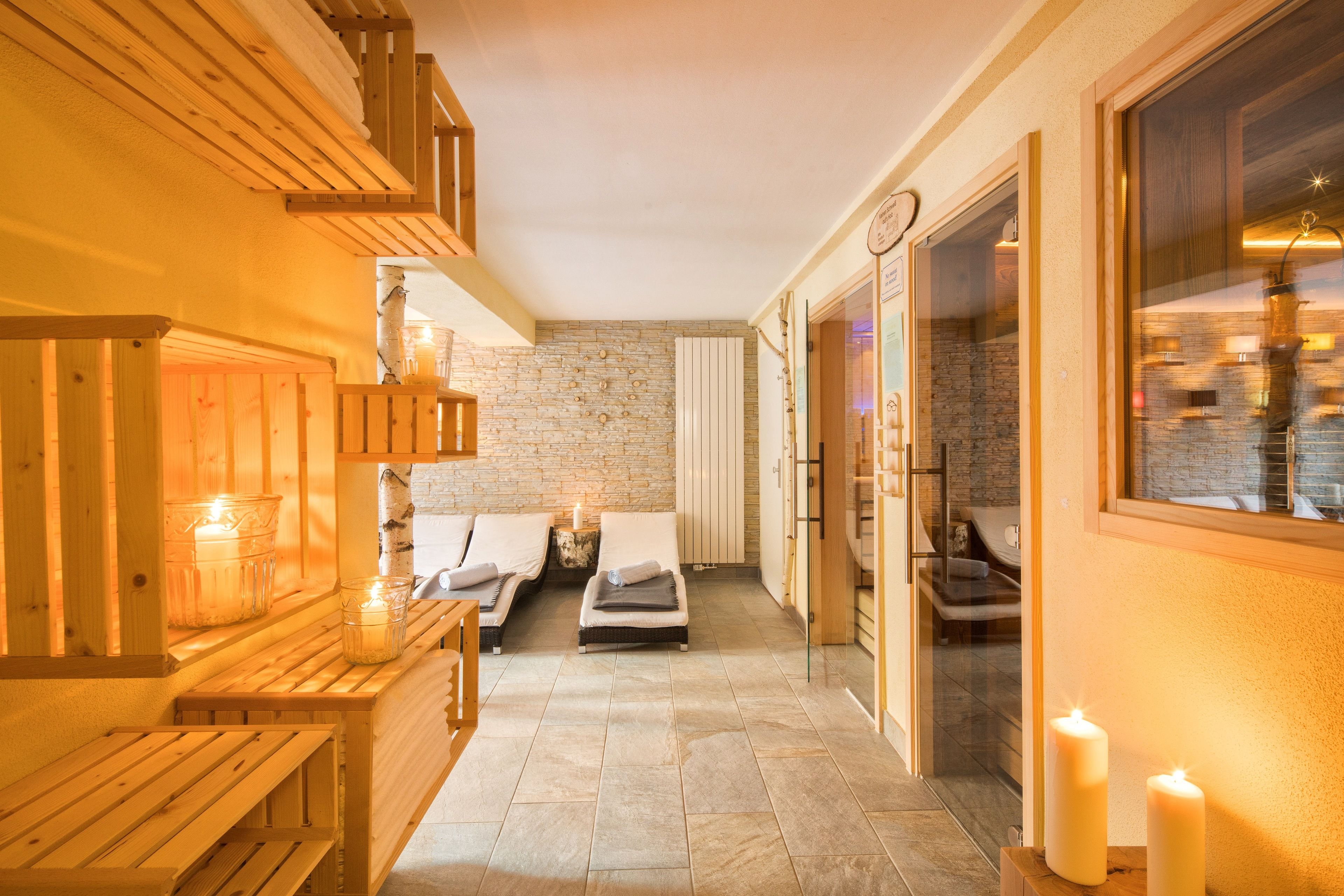 Ein Wellnessbereich mit Holzliegen, zwei Massagesesseln und Kerzen.