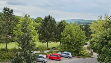 A parking area with three cars, surrounded by trees and a grassy field.