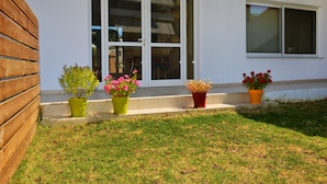 A modern building with a white exterior, a wooden fence, and a grassy lawn. There are three potted plants on the steps. - Despoina (Skiathos)
