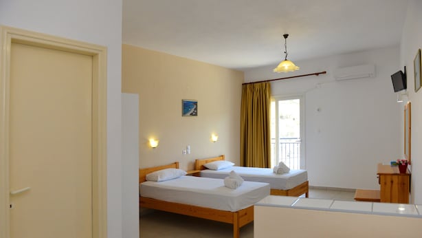 A room with two wooden beds, a small desk, a mirror, and a window with curtains. - Despoina (Skiathos)