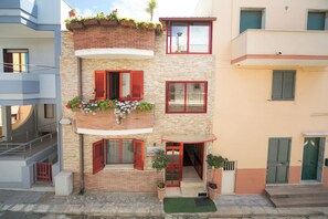 A multi-story building with a brick facade, red shutters, and potted plants on the balconies. - B&B del Lungomare (Gallipoli)