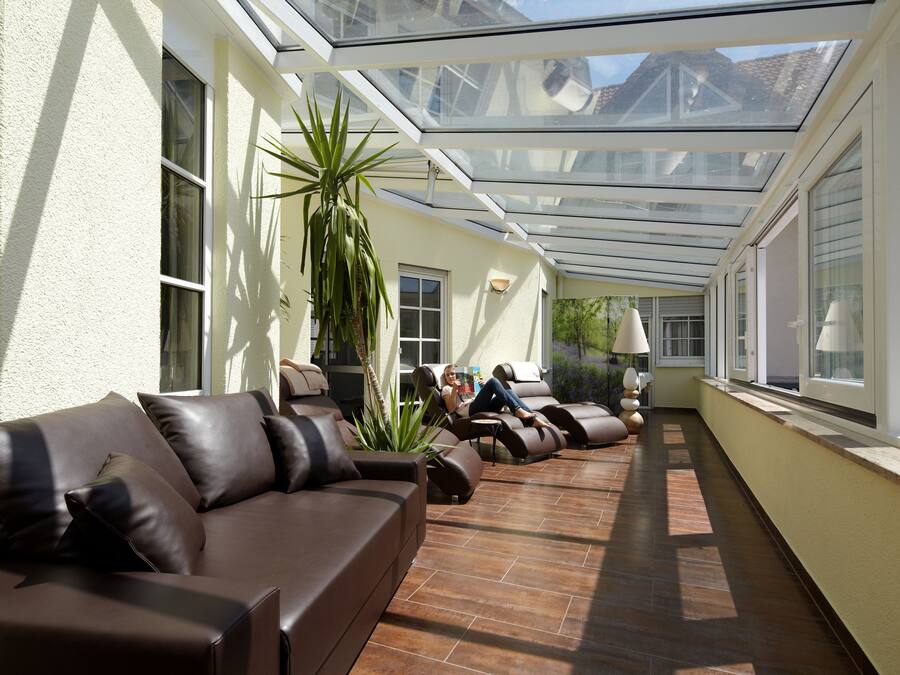 A sunlit covered patio with leather sofas and a tall plant.