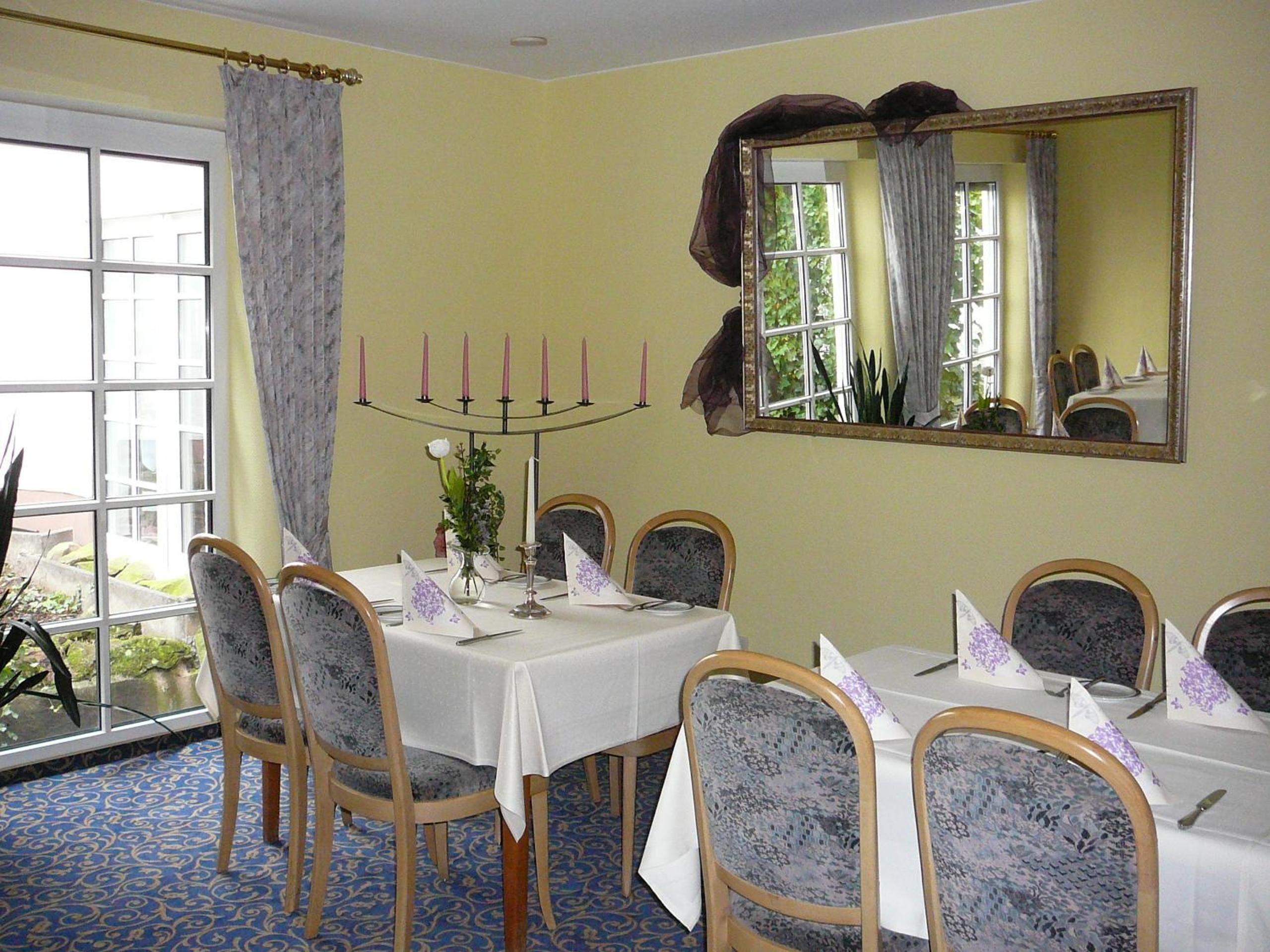 A dining room with a table set for six, chairs with patterned upholstery, a candelabra with candles, and a large mirror on the wall.