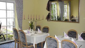 A dining room with a table set for six, chairs with patterned upholstery, a candelabra with candles, and a large mirror on the wall.