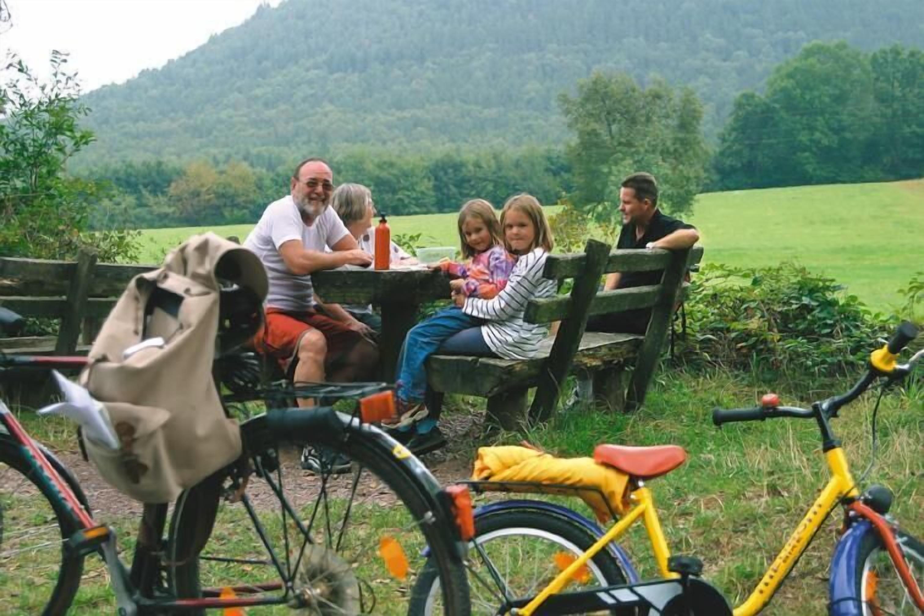 A group of people sitting at a wooden table outdoors with bicycles nearby.