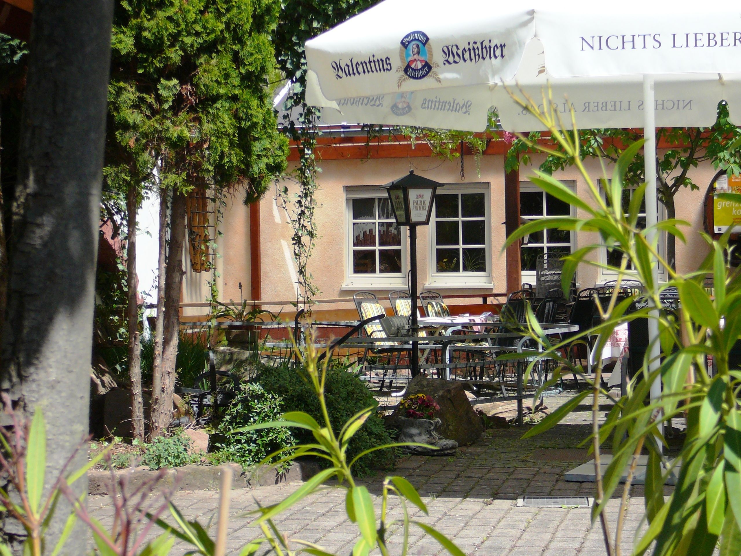 An outdoor seating area with tables and chairs, a stone pathway, and a building with a sign that reads "Valentin's Weisbier."
