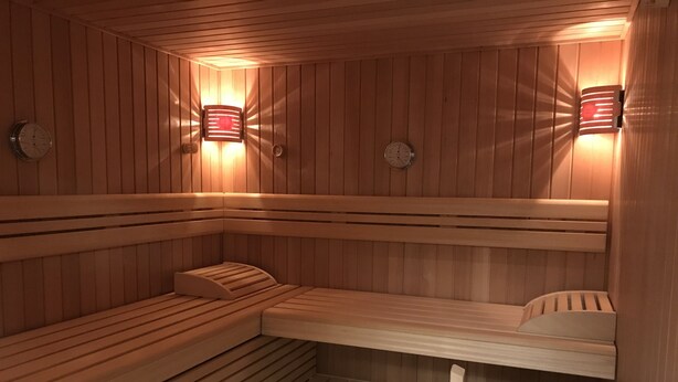 Un sauna avec des bancs en bois, des horloges fixées au mur et des luminaires fixés au mur.